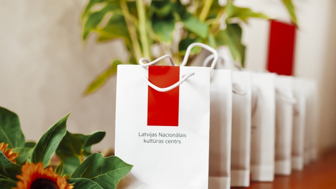 Balti papīra maisiņi ar Latvijas Nacionālā kultūras centra logotipu un saulespuķes