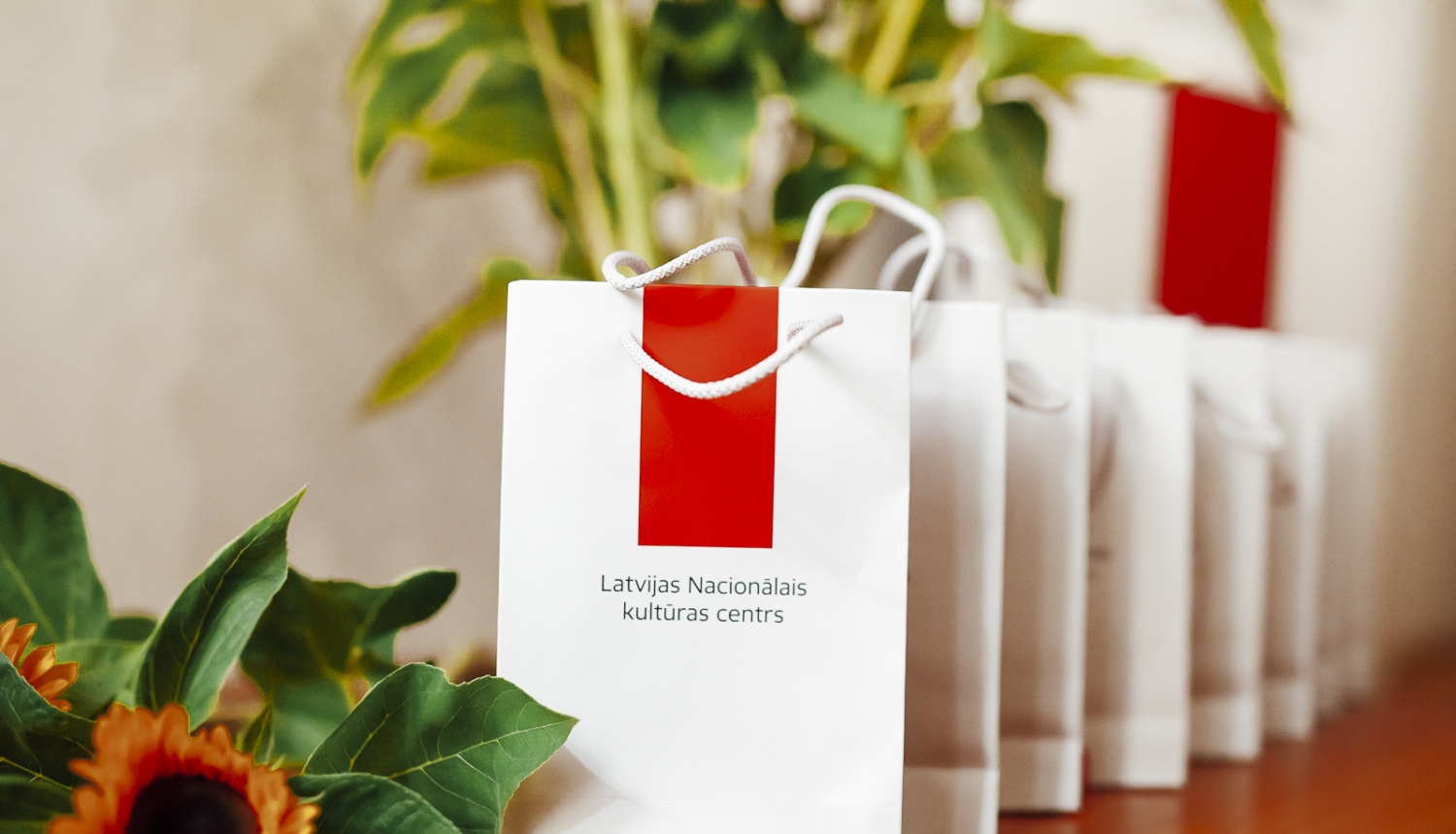 Balti papīra maisiņi ar Latvijas Nacionālā kultūras centra logotipu un saulespuķes