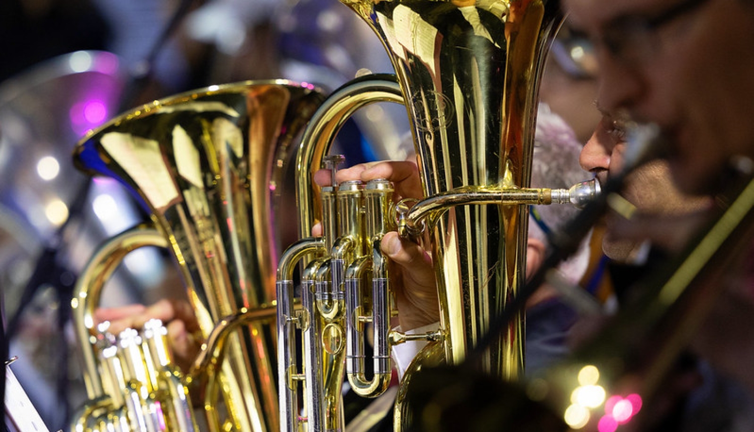 Attēlā redzams pūtēju orķestra muzikants, kurš spēlē lielu vara pūšaminstrumentu'.