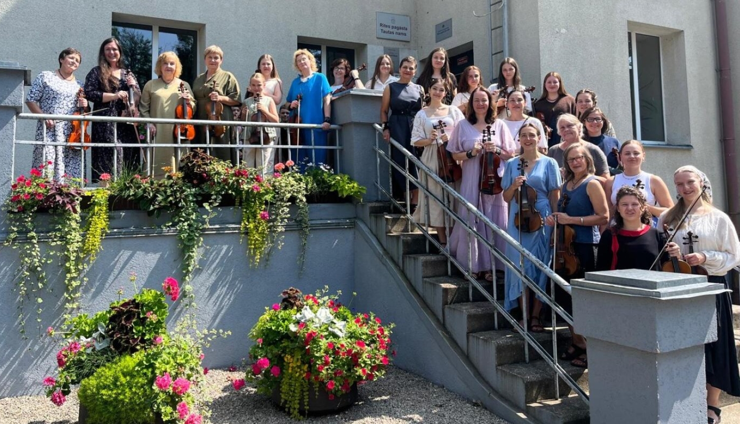 Vijolnieces ar vijolēm rokās stāv uz Rites pagasta Tautas nama kāpnēm