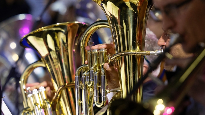Attēlā redzams pūtēju orķestra muzikants, kurš spēlē lielu vara pūšaminstrumentu'.