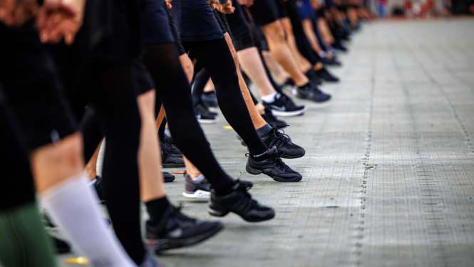 tuvplānā skatuviskās dejas dejotāju kājas sper vienotu soli stadionā deju svētku mēģinājumā