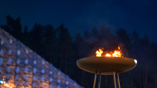 Lielā melnā metāla traukā redzamas uguns liesmas. Tas ir daļa no Dziesmu svētku scenogrāfijas Mežaparka Lielajā estrādē