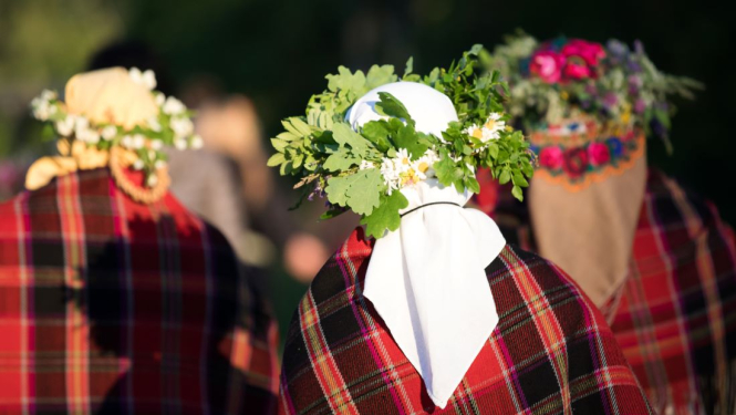 Trīs sievas tautas tērpos ar lakatiem un vainagiem