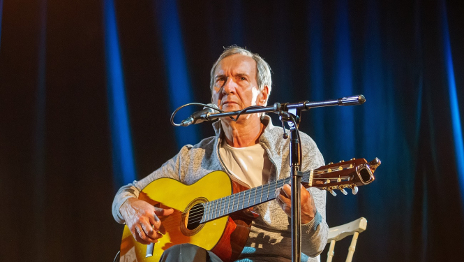 vīrietis ar ģitāru dzied pie mikrofona