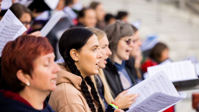 Kora dziedātāji no nošu mapēm dzied estrādē