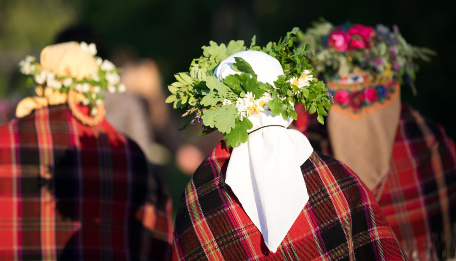 Trīs sievas tautas tērpos ar lakatiem un vainagiem