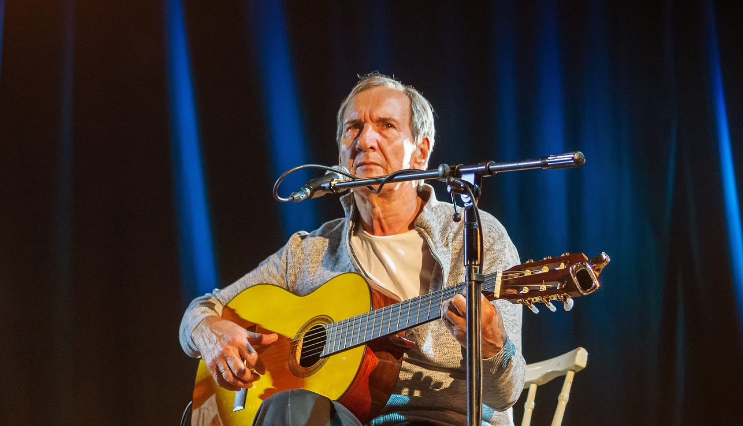 vīrietis ar ģitāru dzied pie mikrofona