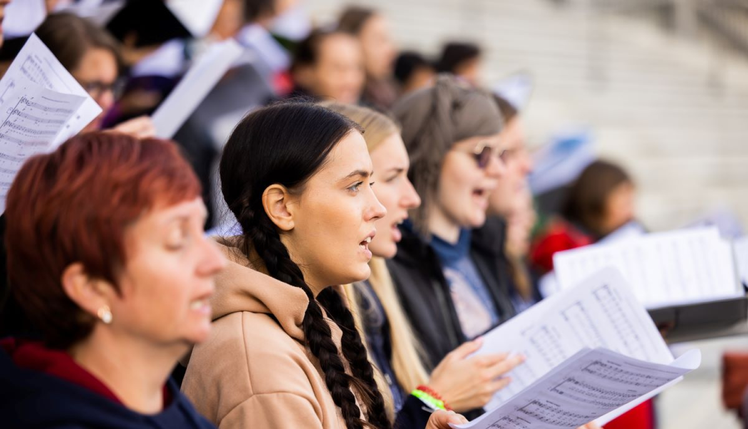 Kora dziedātāji no nošu mapēm dzied estrādē