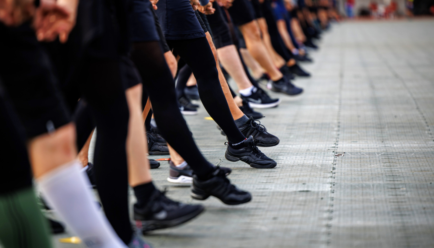 tuvplānā skatuviskās dejas dejotāju kājas sper vienotu soli stadionā deju svētku mēģinājumā